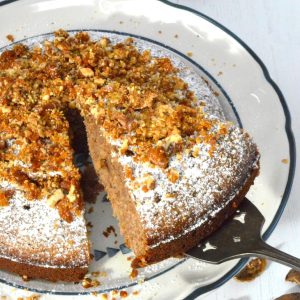A slice of Greek walnut cake topped with praline being removed from the main bake.