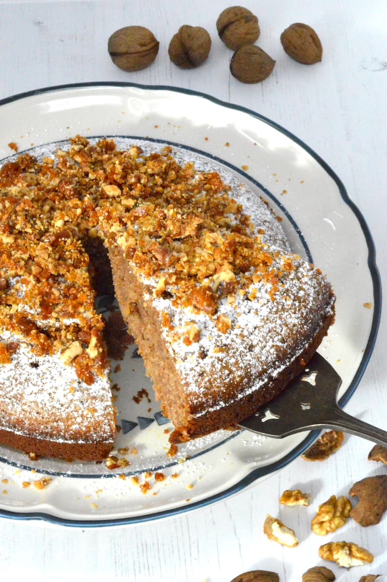 A slice of Greek walnut cake topped with praline being removed from the main bake.