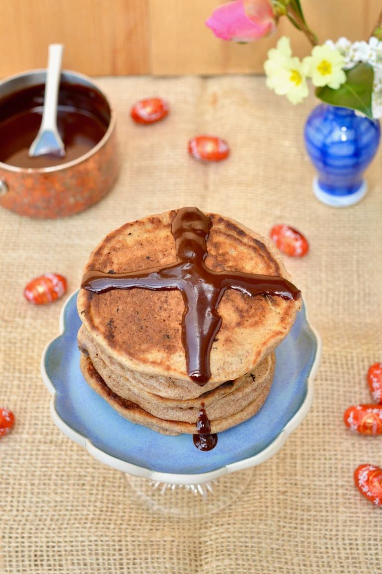 A stack of hot cross bun pancakes with a chocolate sauce cross on top.