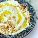 A bowl of whipped feta with garlic and parsley. Topped with olive oil and toasted pine nuts.
