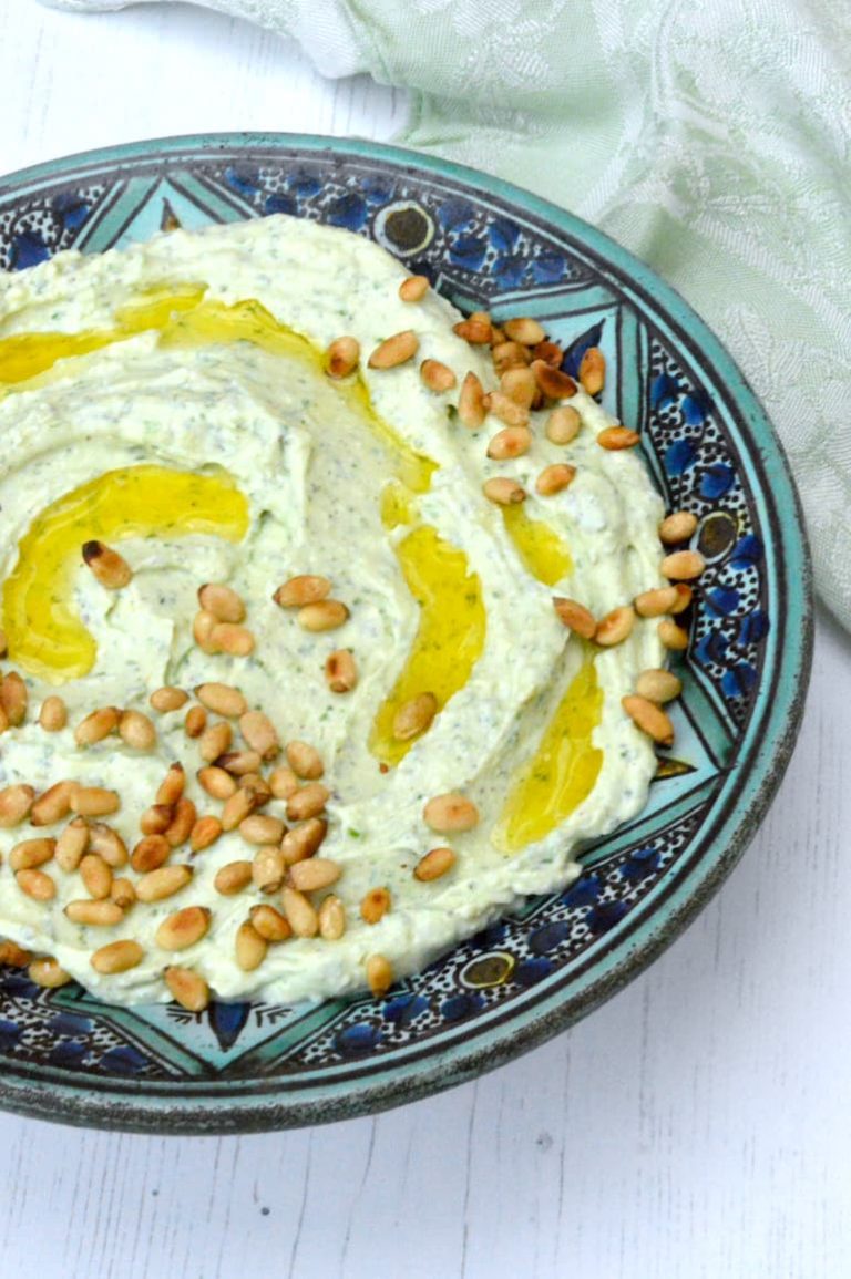 A bowl of whipped feta with garlic and parsley. Topped with olive oil and toasted pine nuts.