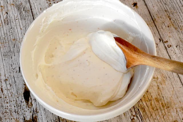 Cream cheese icing in bowl with wooden spoon.