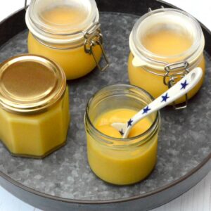 Four jars of homemade grapefruit curd, one open with spoon inside.