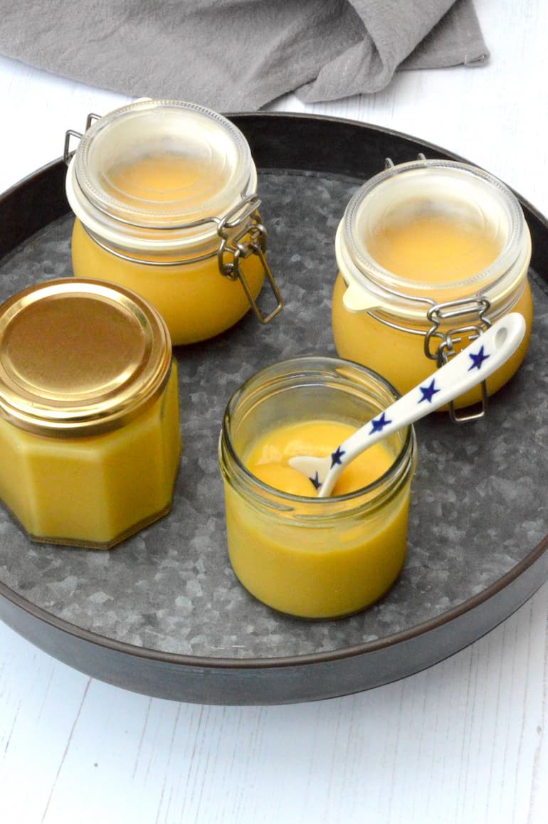 Four jars of homemade grapefruit curd, one open with spoon inside.
