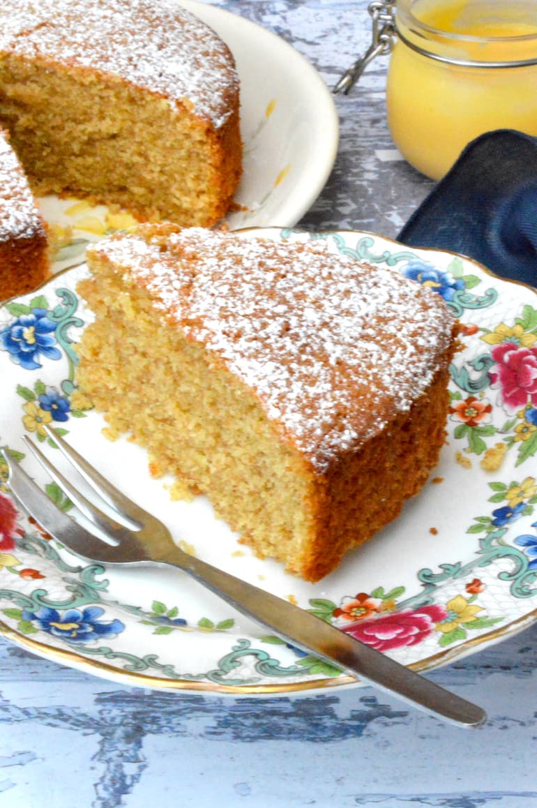 A slice of simple lemon curd cake to the fore with a jar of lemon curd behind.