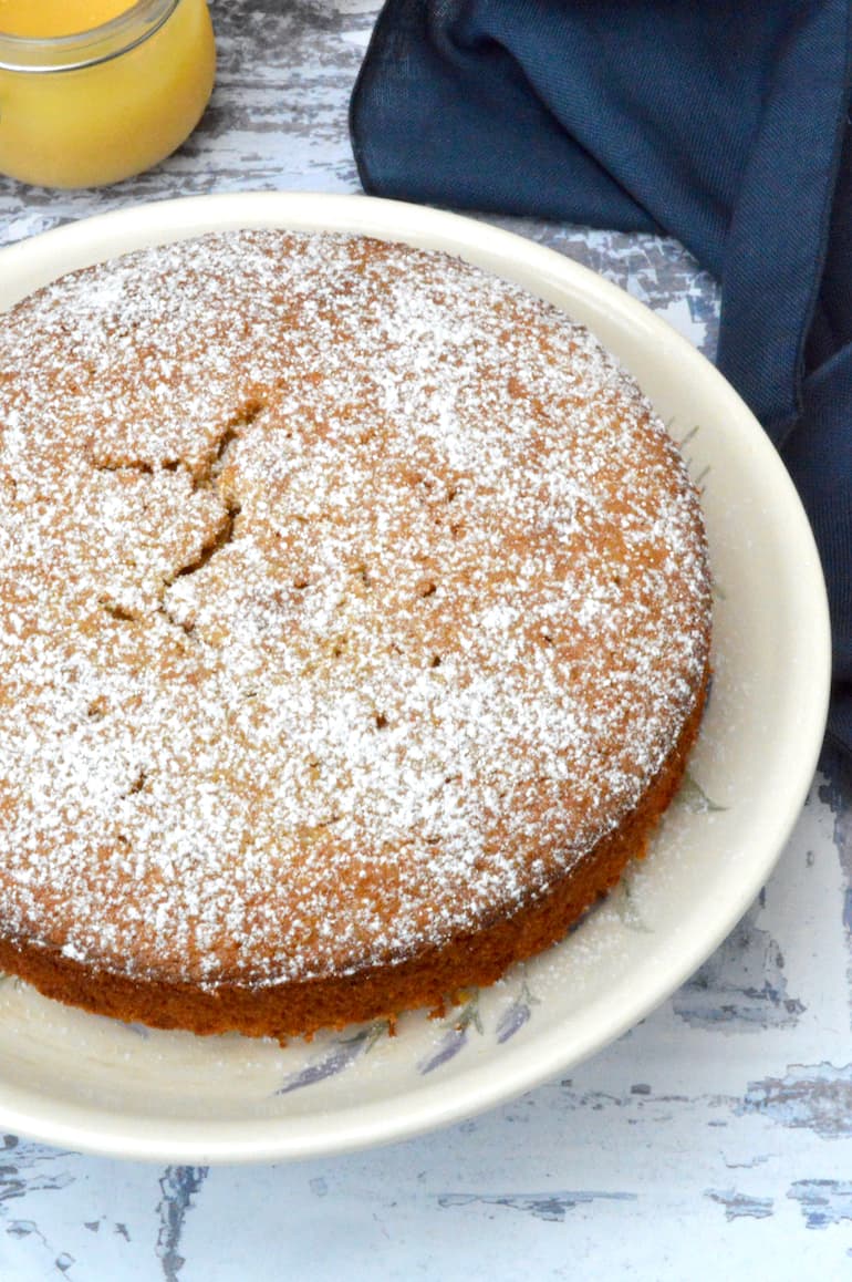 Simple lemon curd cake dusted with icing sugar on plate.