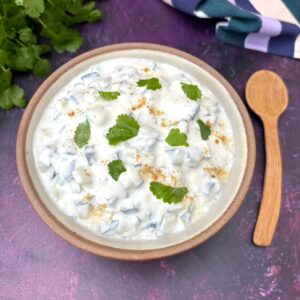 A bowl or simple raita with wooden spoon and coriander leaves.
