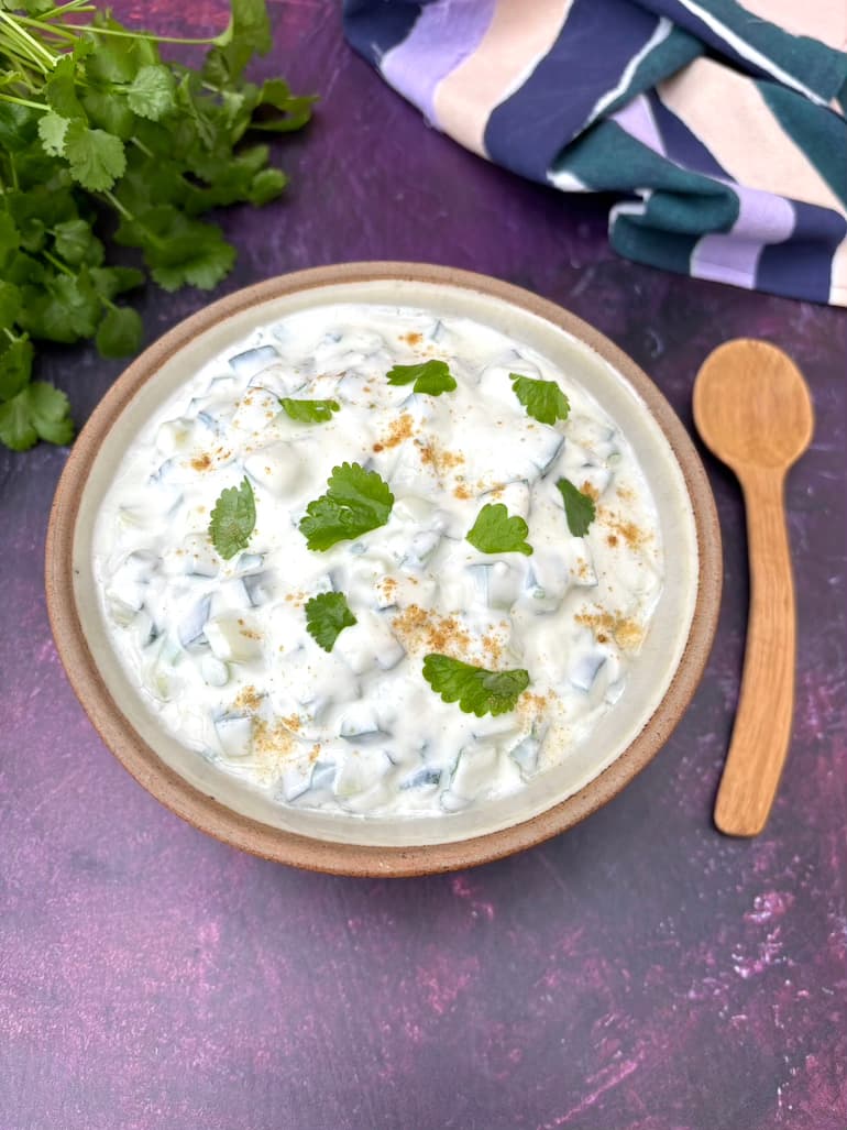 A bowl or simple raita with wooden spoon and coriander leaves.