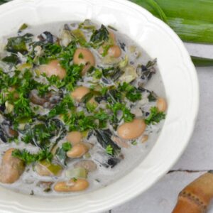 Partial view of a bowl of creamy butter beans with mushrooms, leeks and wild greens.