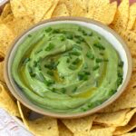 Bowl of vegan green dip with tortilla chips.