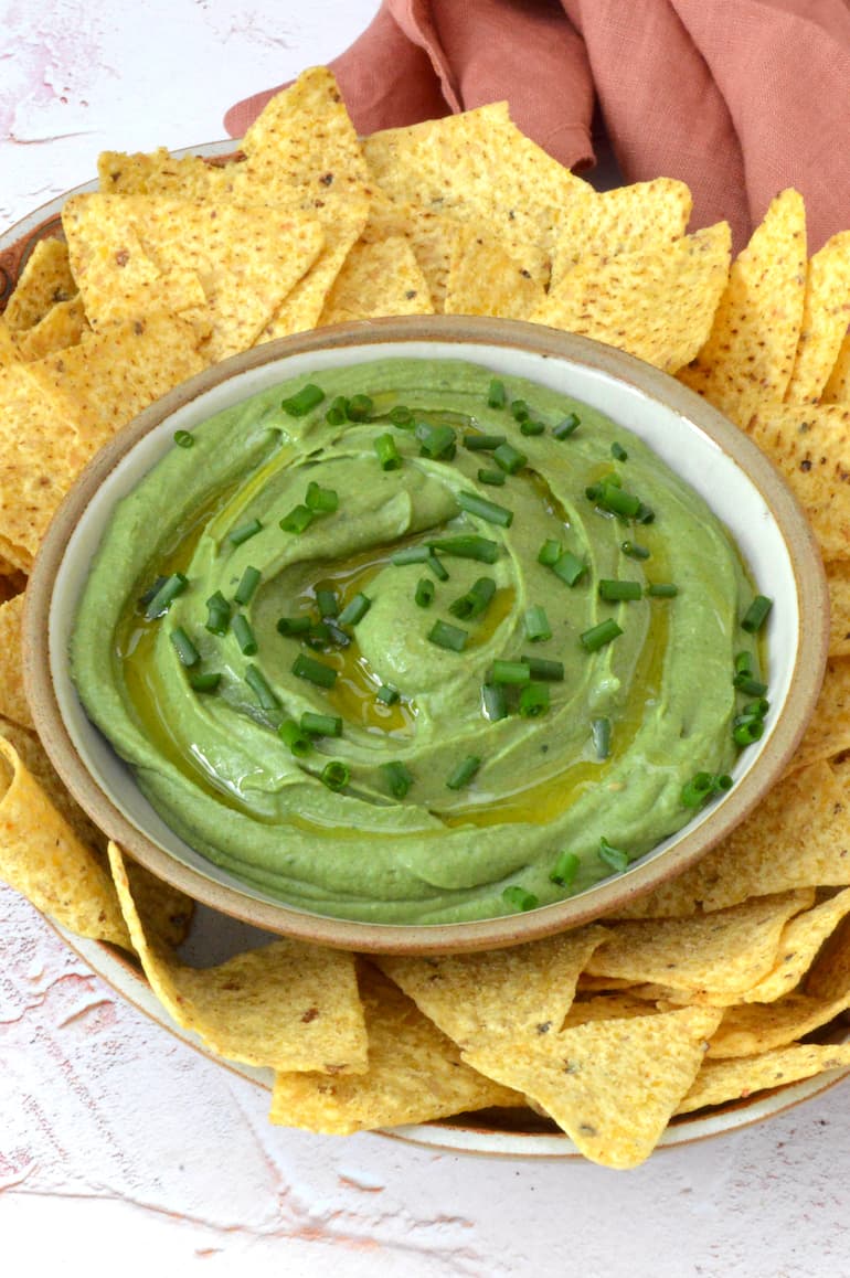 Bowl of vegan green dip with tortilla chips.