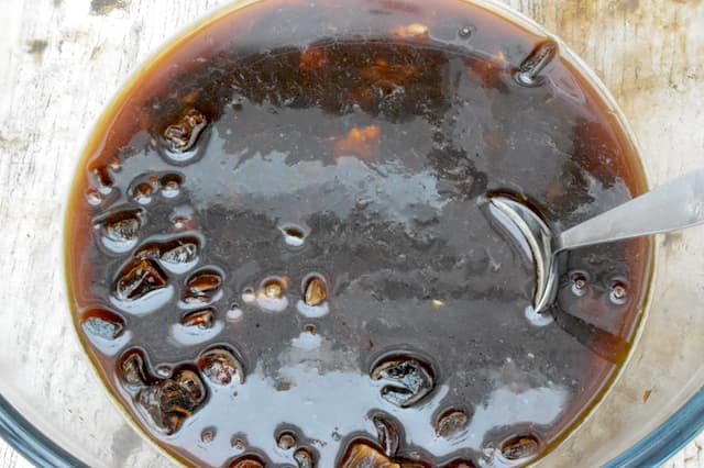 Tea poured over dried fruit in glass bowl with spoon.