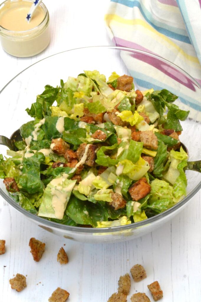 Tempeh caesar salad in bowl with dressing on side.