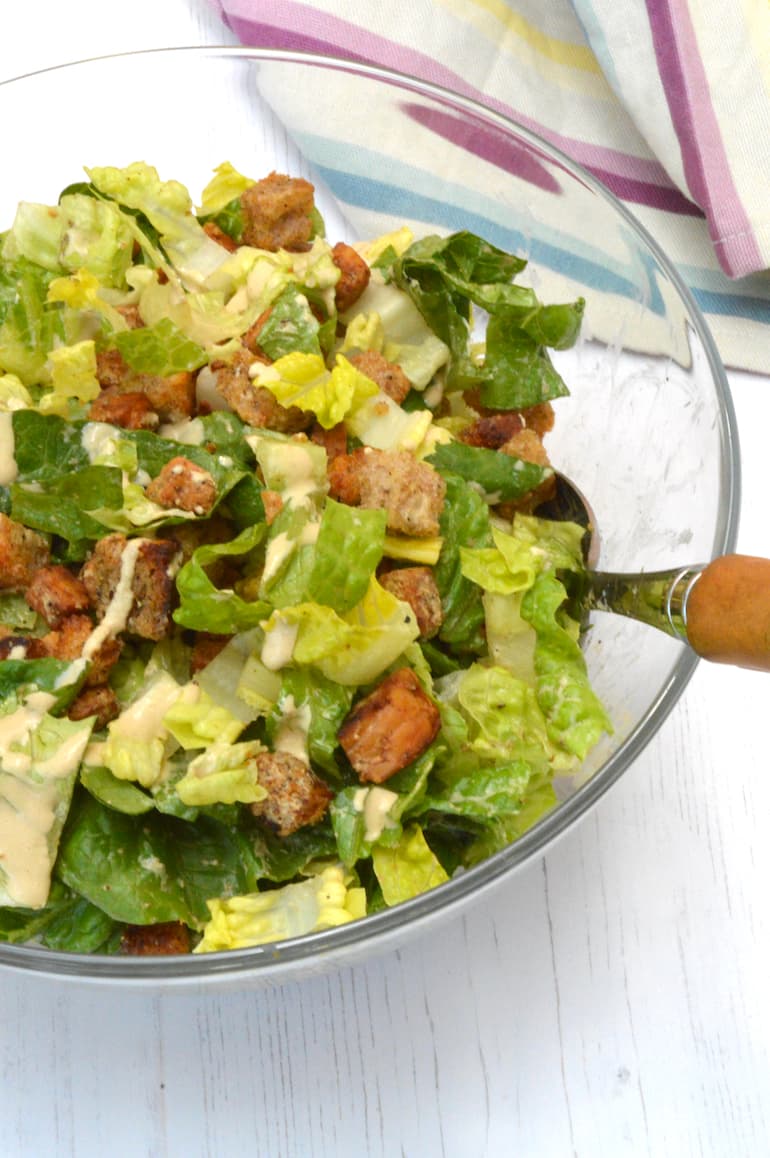 Close up of tempeh caesar salad in glass bowl with spoon.