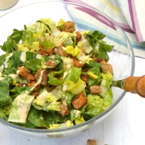 Tempeh caesar salad in glass bowl with dressing on side.