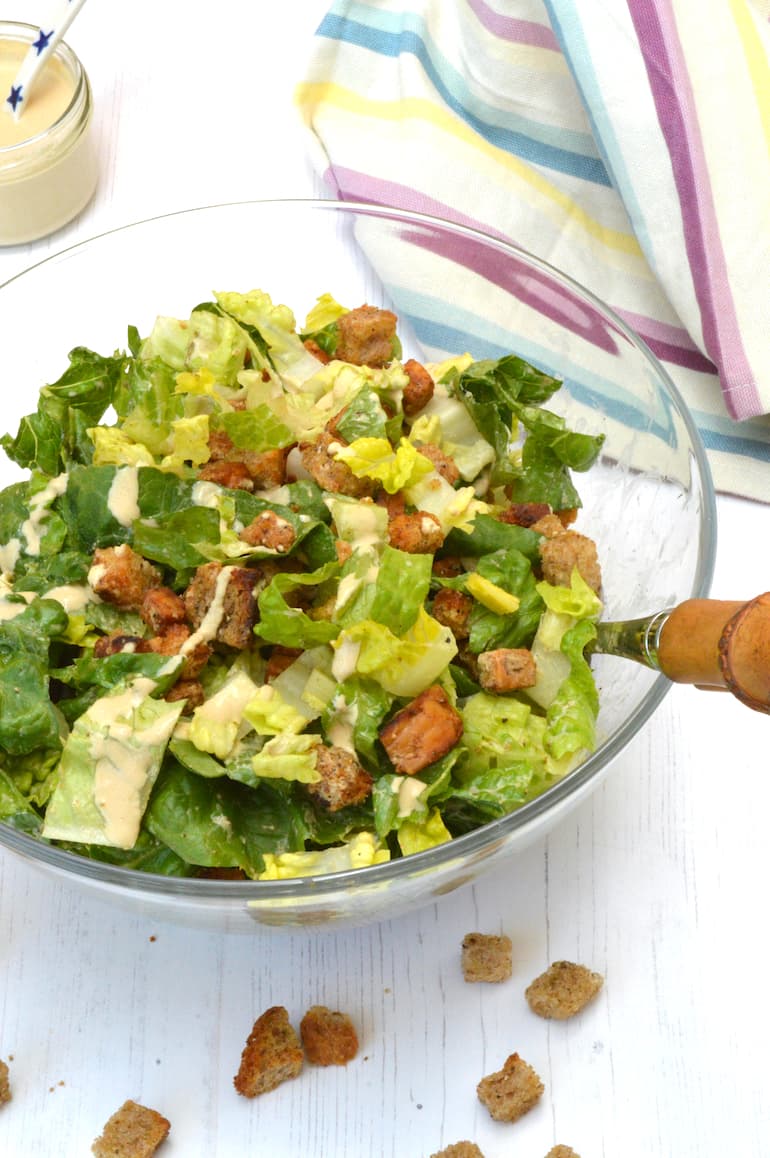 Tempeh caesar salad in glass bowl with dressing on side.