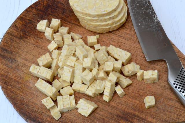 A board of diced tempeh with knife.