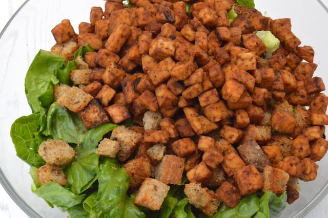 Tempeh, croutons and lettuce in bowl.