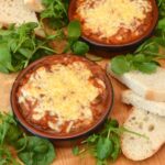 Two individual cheesy bean bakes with bread and green leaves.