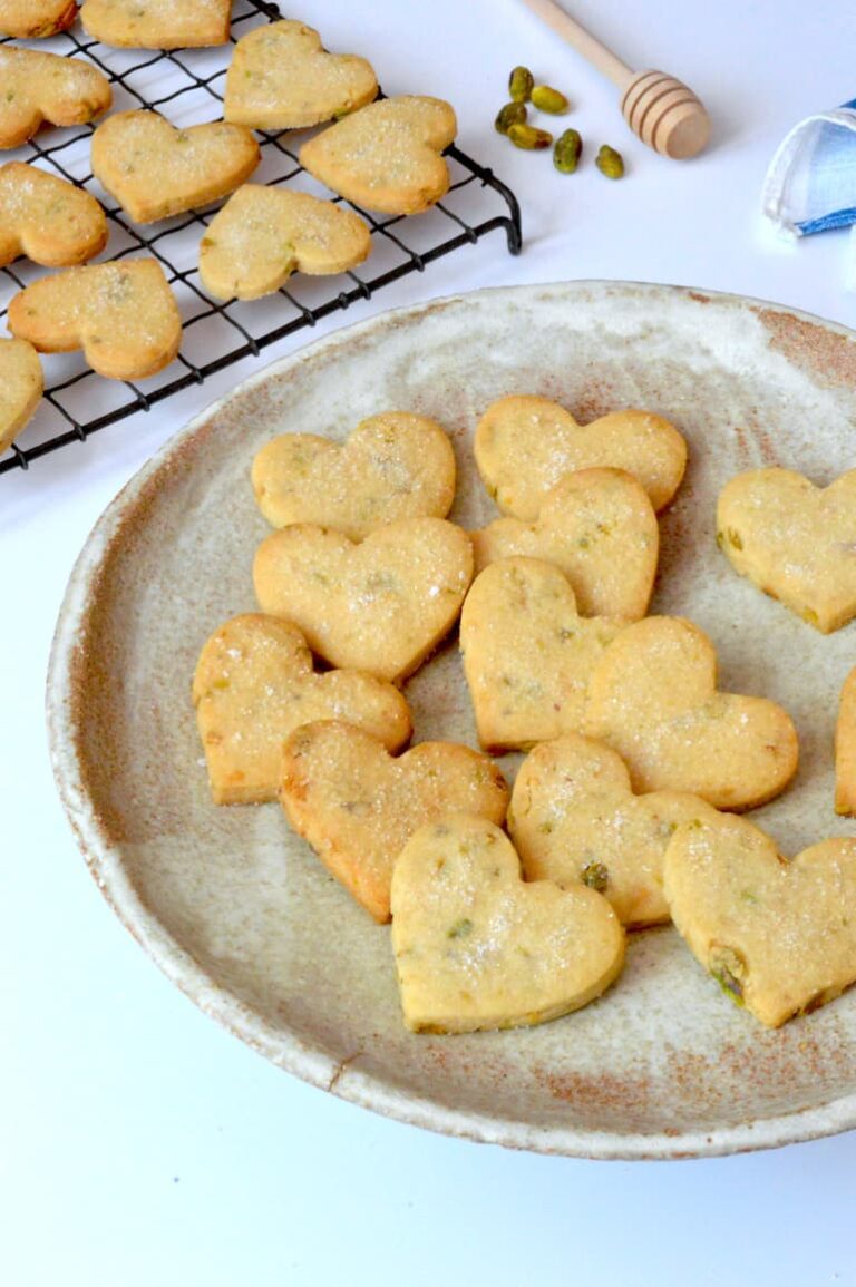 Plate of homemade honey pistachio shortbread hearts with more on rack.