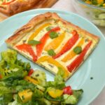 Sweet pepper tart slice on plate with green salad.