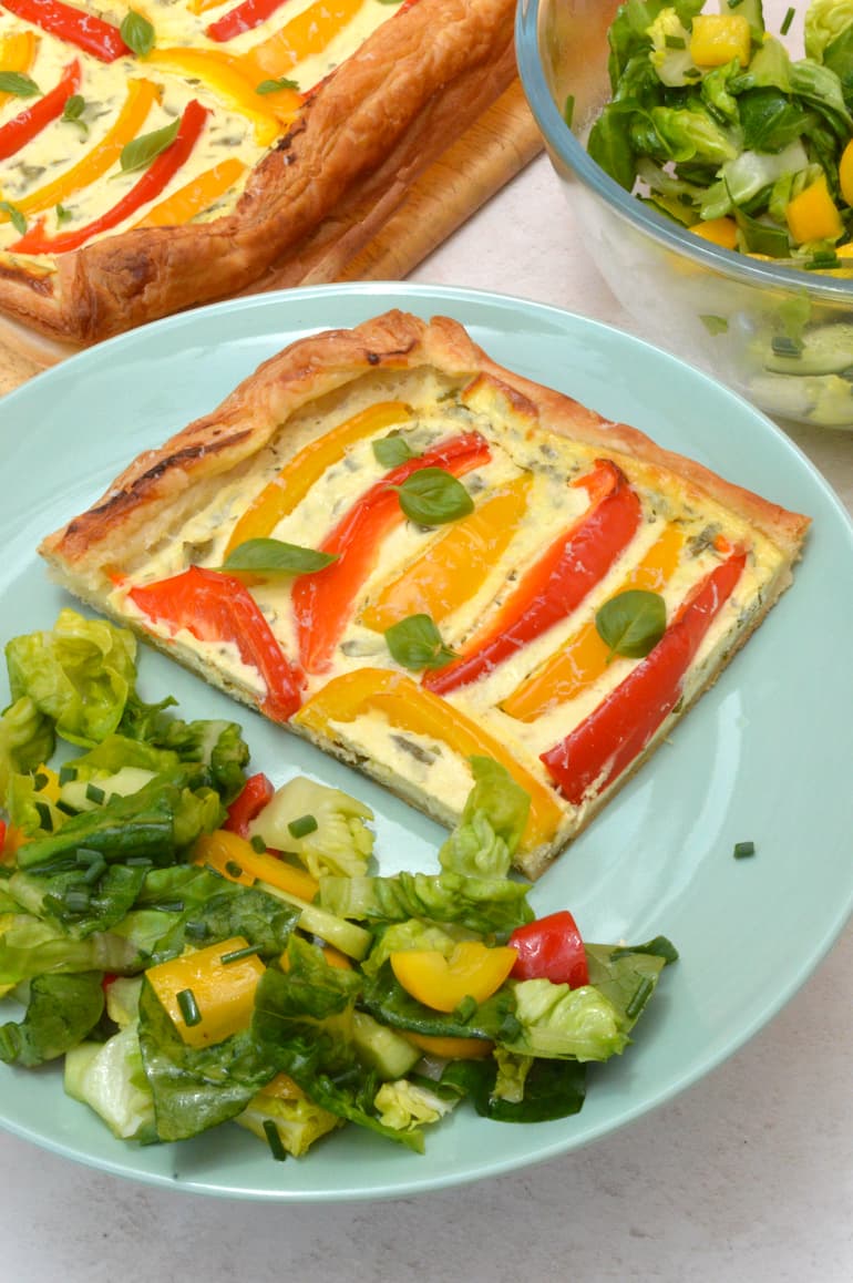 Sweet pepper tart slice on plate with green salad.