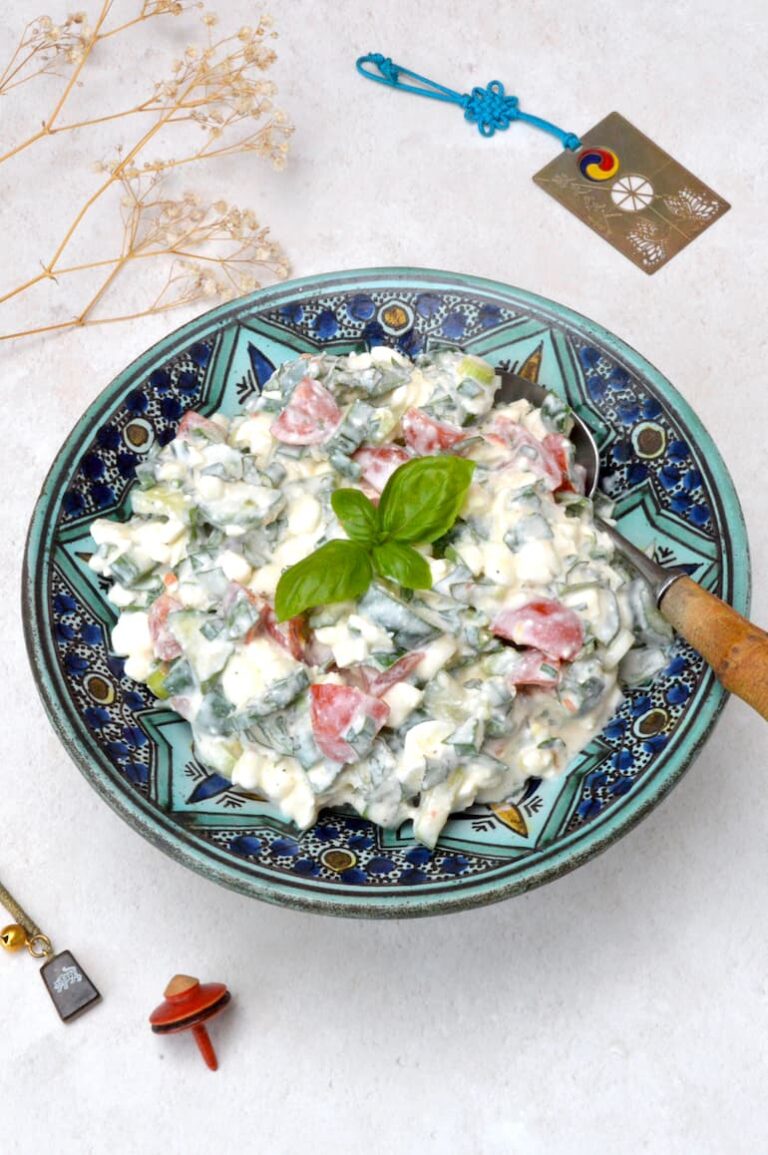 A bowl of cottage cheese salad with cucumber, tomatoes and fresh herbs.