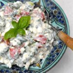 A bowl of cottage cheese salad with spoon and basil sprig.
