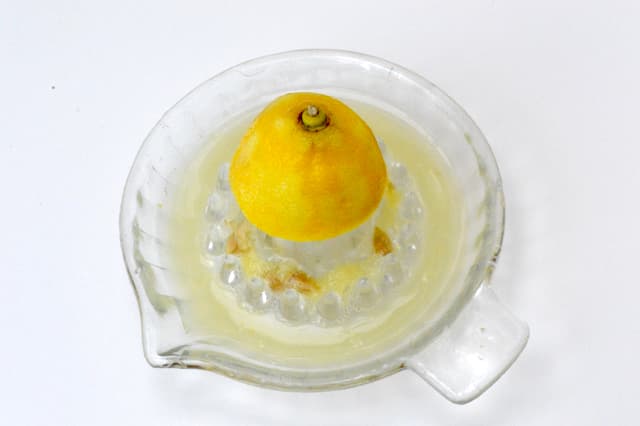 Half lemon being juiced in glass squeezer.