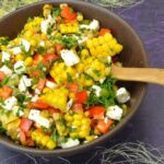 Bowl of corn salad with feta, peppers and parsley.