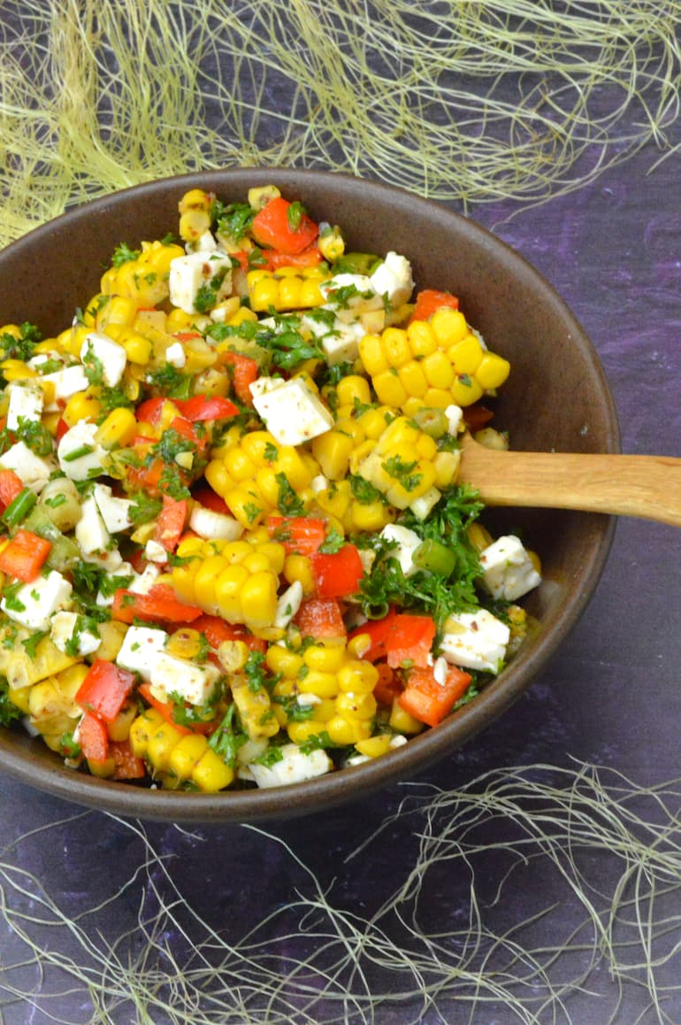 Bowl of corn salad with feta, peppers and parsley.