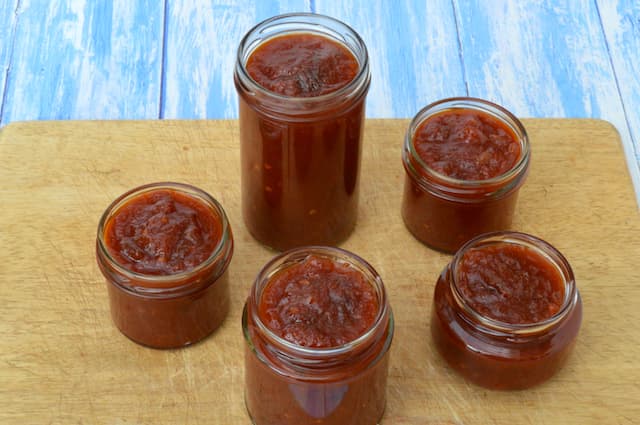 Five open jars of chilli and tomato chutney.
