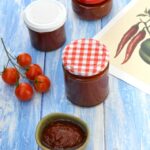 Three jars of chilli and tomato chutney, plus some in small open bowl.