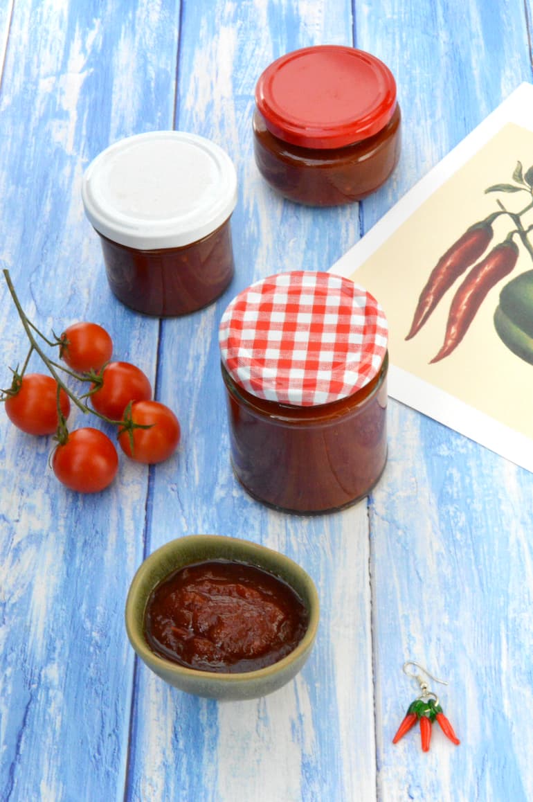 Three jars of chilli and tomato chutney, plus some in small open bowl.
