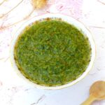 Bowl of homemade green zhoug with wooden spoon on side.
