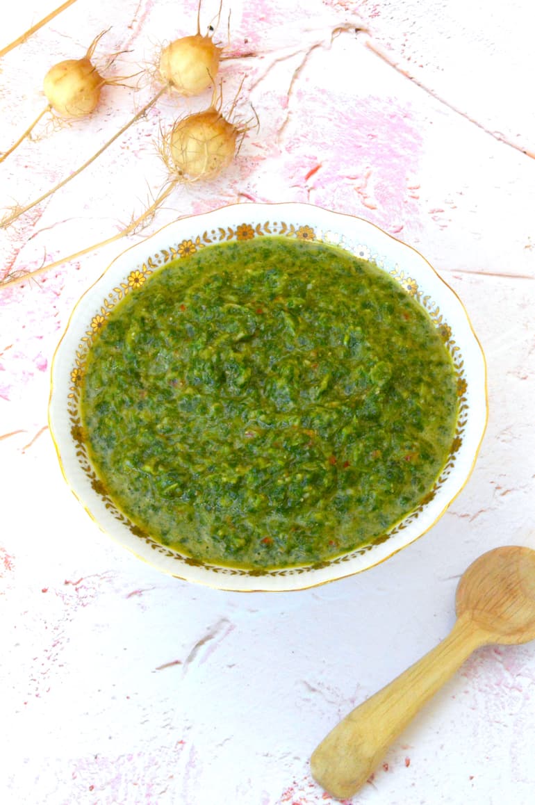 Bowl of homemade green zhoug with wooden spoon on side.