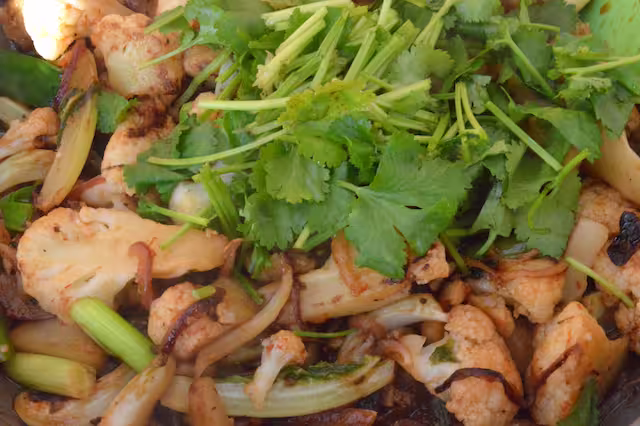 Coriander leaves added to stir-fry pan.