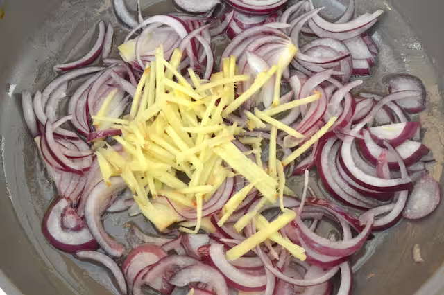 Ginger matchsticks added to frying red onions in pan.