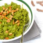 Partial bowl of pasta covered in green kale sauce with tofu and fork.