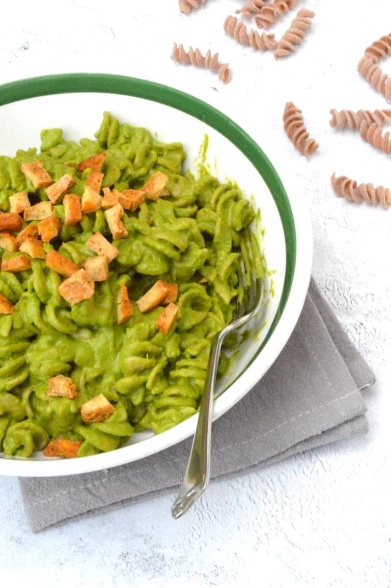 Partial bowl of pasta covered in green kale sauce with tofu and fork.
