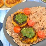 Two carrot and chickpea fritters on flatbread with green sauce and halved tomatoes.