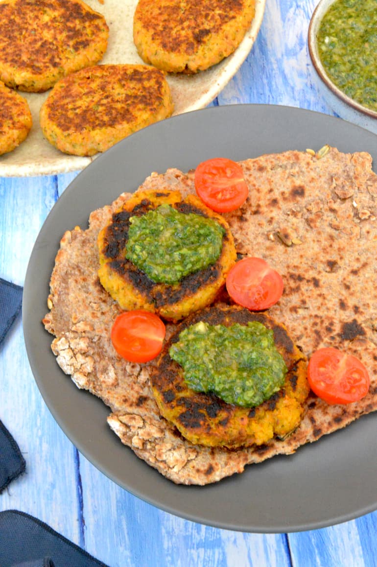 Two carrot and chickpea fritters on flatbread with green sauce and halved tomatoes.