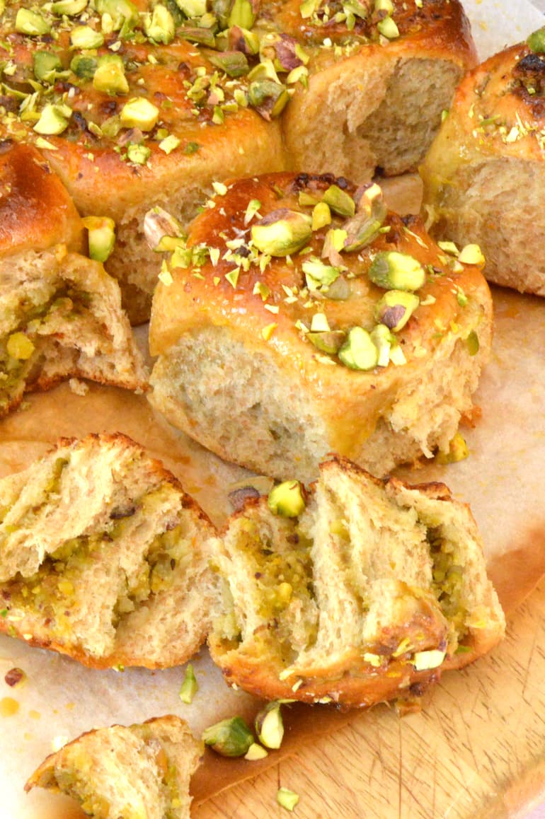 Homemade sticky orange pistachio yeasted buns with one torn open.