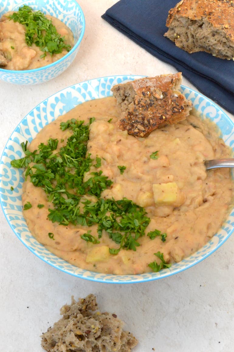 Bowl of creamy tahini white beans with bread and parsley.