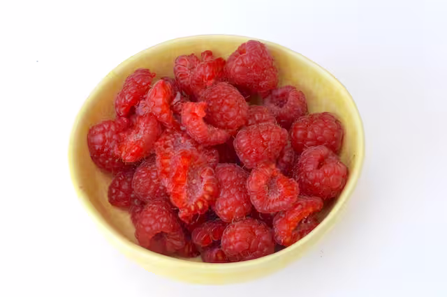 Bowl of raspberries with larger ones halved.