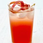Rhubarb cocktail in a tumbler glass with ice and knot of rhubarb on top.