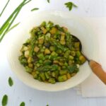 Bowl of spring vegetable medley with spoon and herbs.