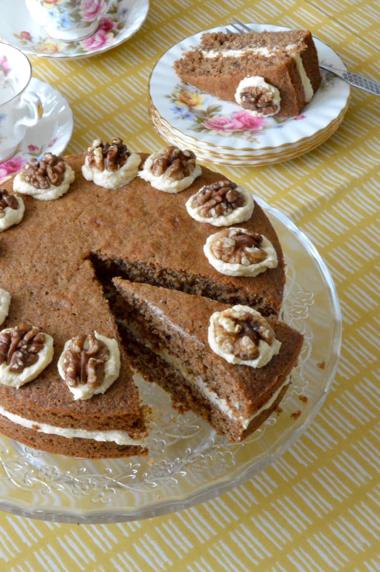 Coffee and walnut cake on stand with slice on plate alongside.