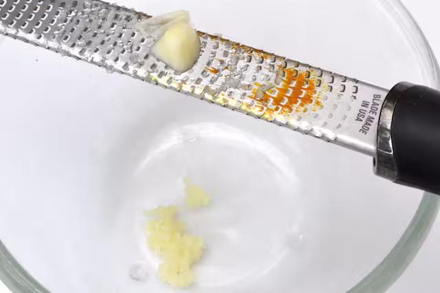 Grating garlic into bowl with microplane.