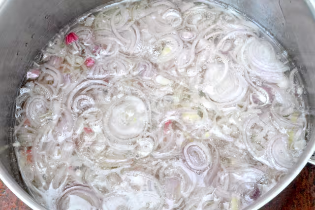 Sliced shallots added to hot oil in pan.